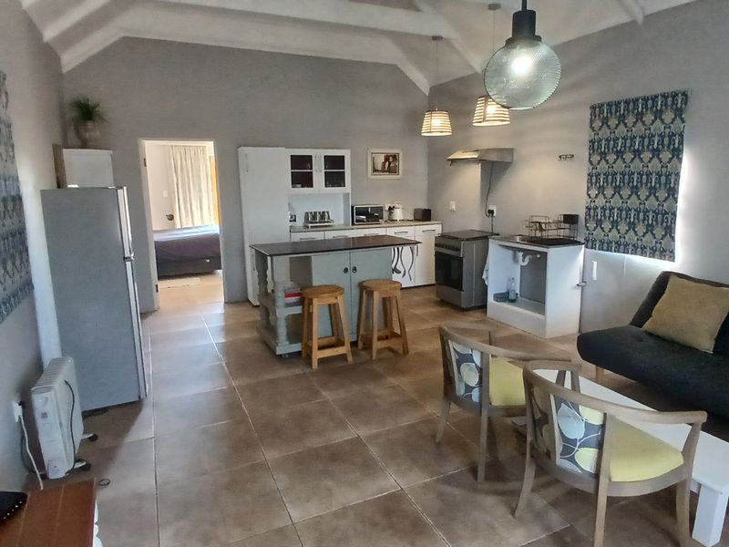 Open-plan living area featuring a vaulted ceiling with exposed beams, tiled flooring, and a functional kitchen with a central island and built-in cabinetry.