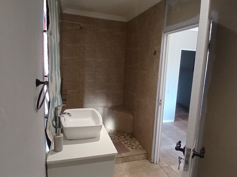 A functional bathroom featuring a vessel sink vanity and a tiled walk-in shower with a built-in bench.