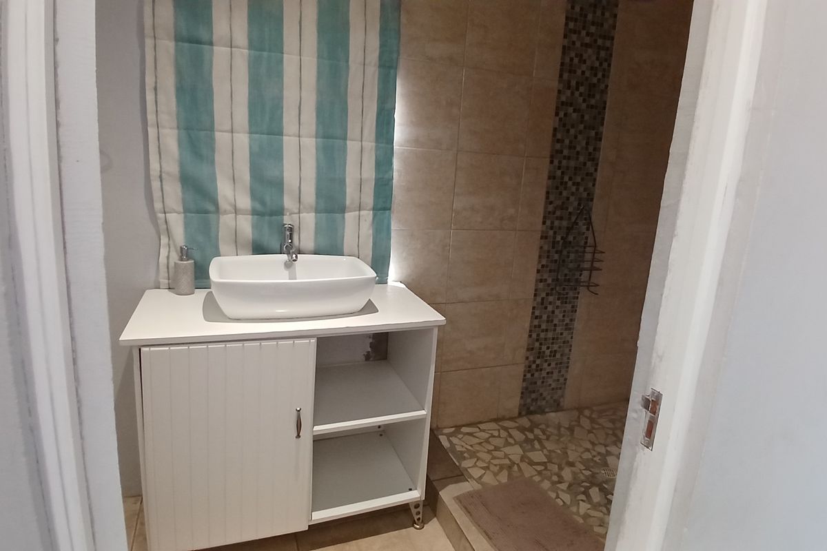 A functional bathroom featuring a modern vessel sink on a white vanity cabinet and a walk-in shower with mosaic tile accents.