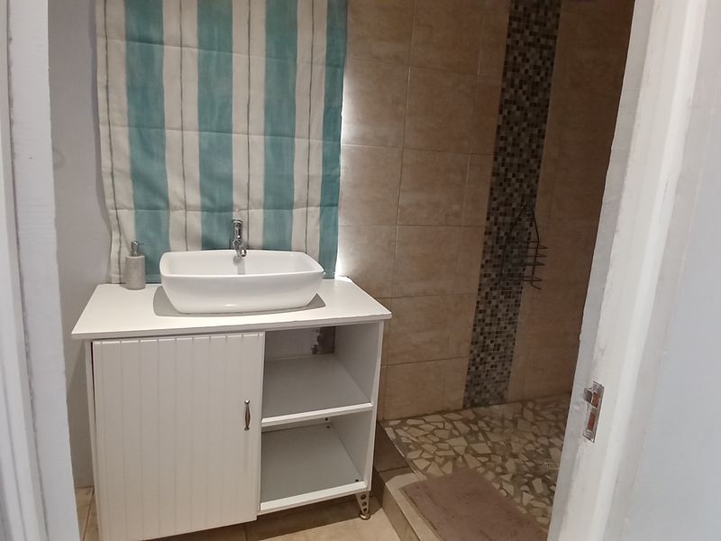 A functional bathroom featuring a modern vessel sink on a white vanity cabinet and a walk-in shower with mosaic tile accents.