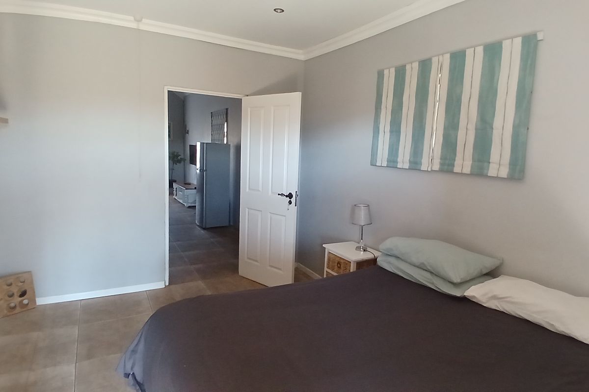 A neutrally painted bedroom featuring tiled flooring, recessed downlighting, and coved ceiling details, with an open doorway leading to an adjacent living space.