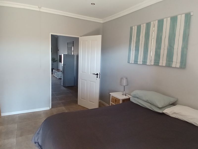 A neutrally painted bedroom featuring tiled flooring, recessed downlighting, and coved ceiling details, with an open doorway leading to an adjacent living space.