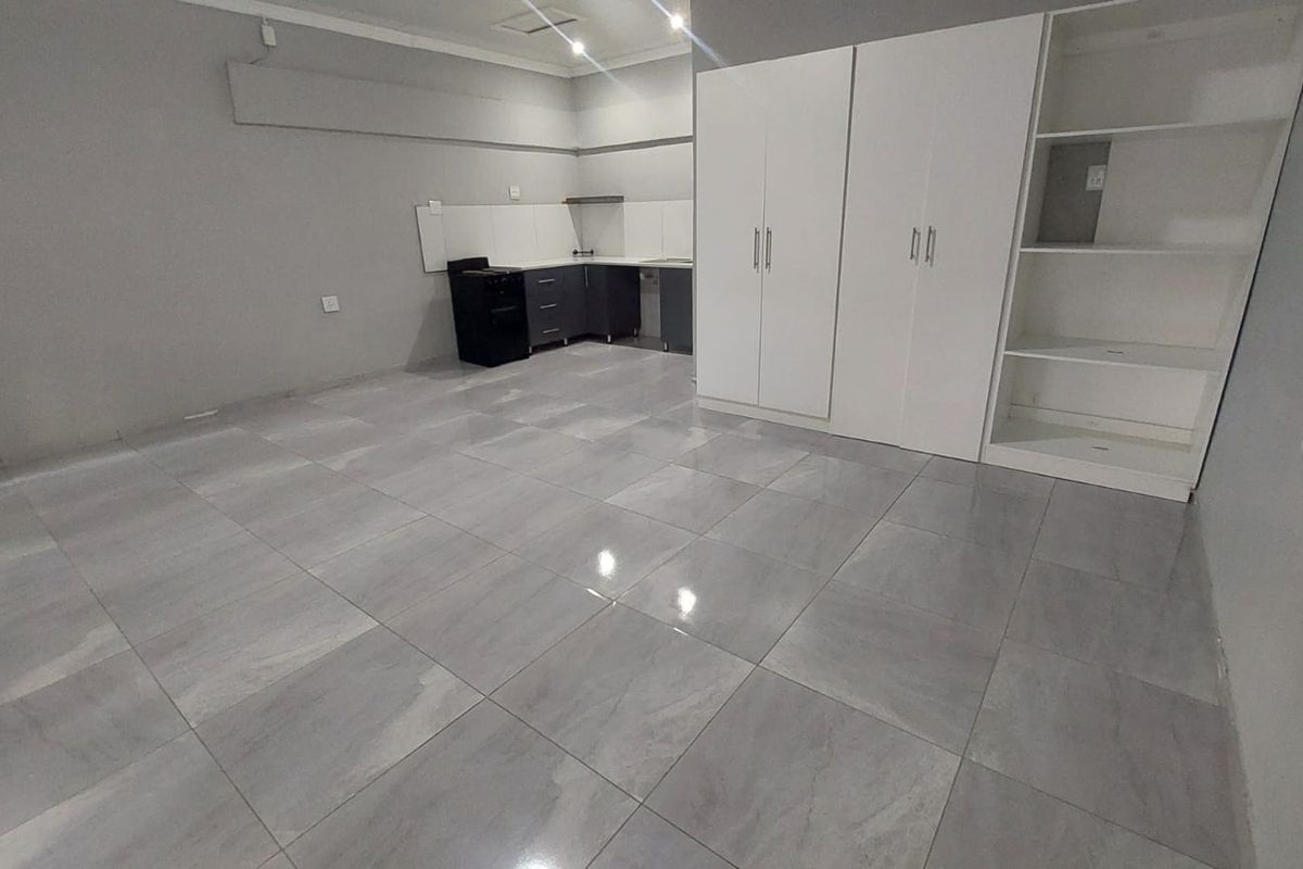An open-plan living area featuring large format floor tiles, built-in storage cupboards, and a compact kitchen corner with modern cabinetry.
