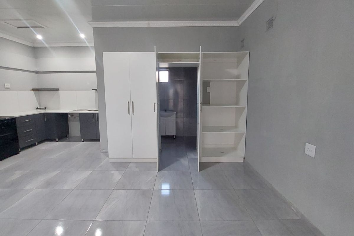 An open-plan living and kitchen area featuring modern grey floor tiles, built-in cabinetry, and a built-in wardrobe, presenting a clean and functional space.