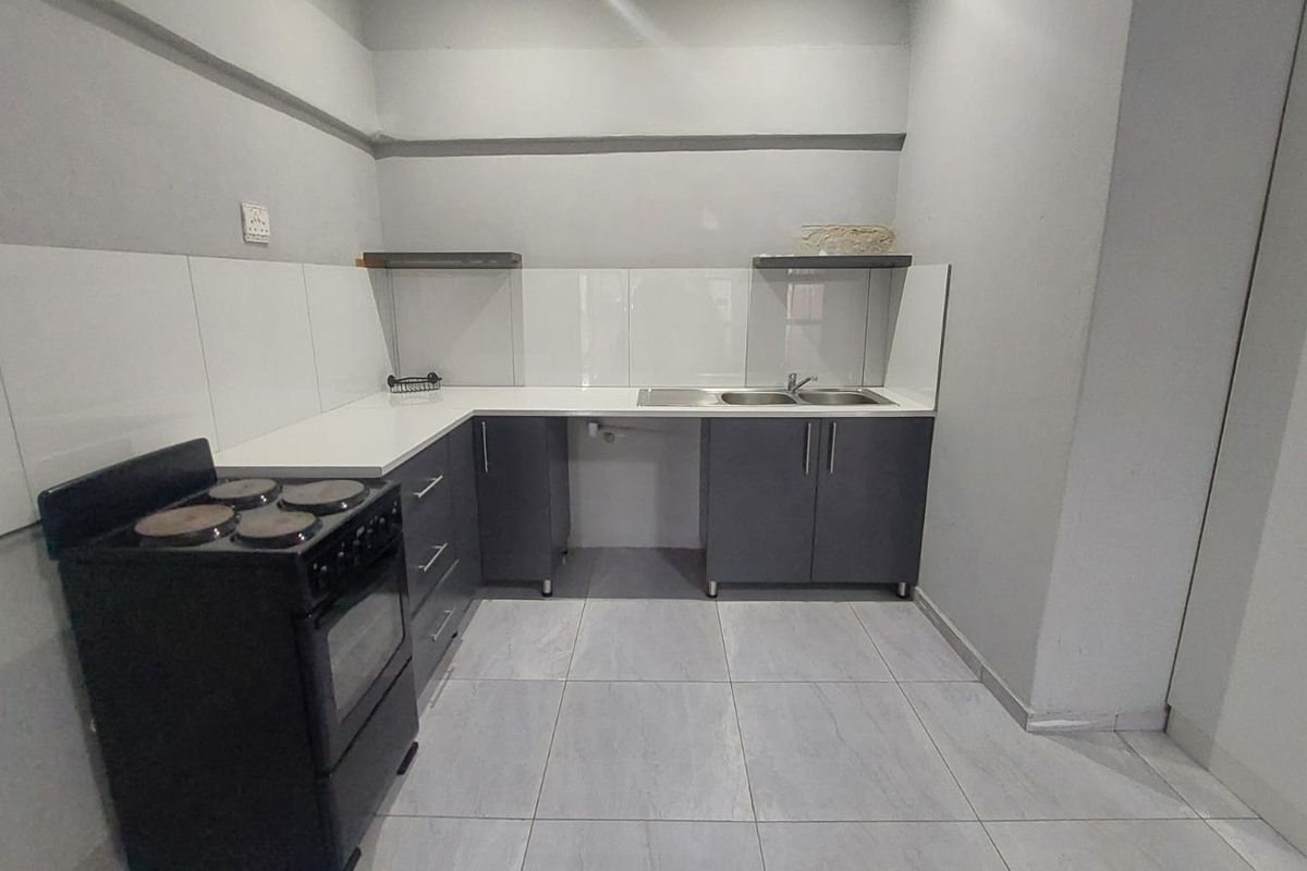 A clean, functional kitchen featuring grey cabinetry, white countertops, a double sink, tiled splashback, and a freestanding stove.
