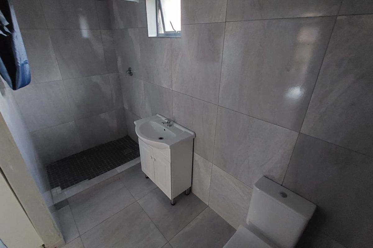 A functional bathroom featuring a walk-in shower, vanity cabinet with basin, and toilet, finished with neutral grey wall and floor tiles.