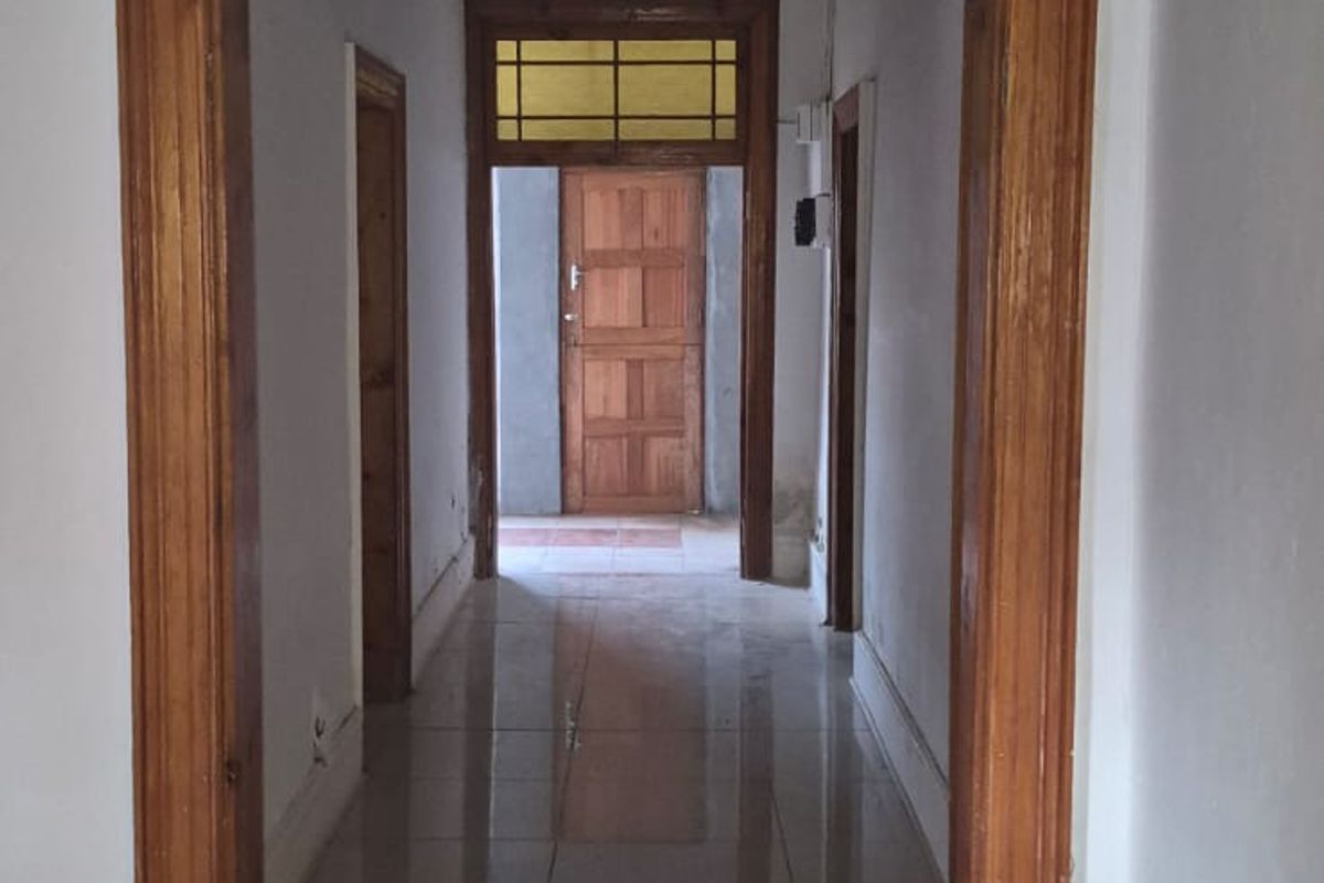 A long, empty hallway featuring tiled flooring, wooden door frames, and a transom window above the rear exit door.