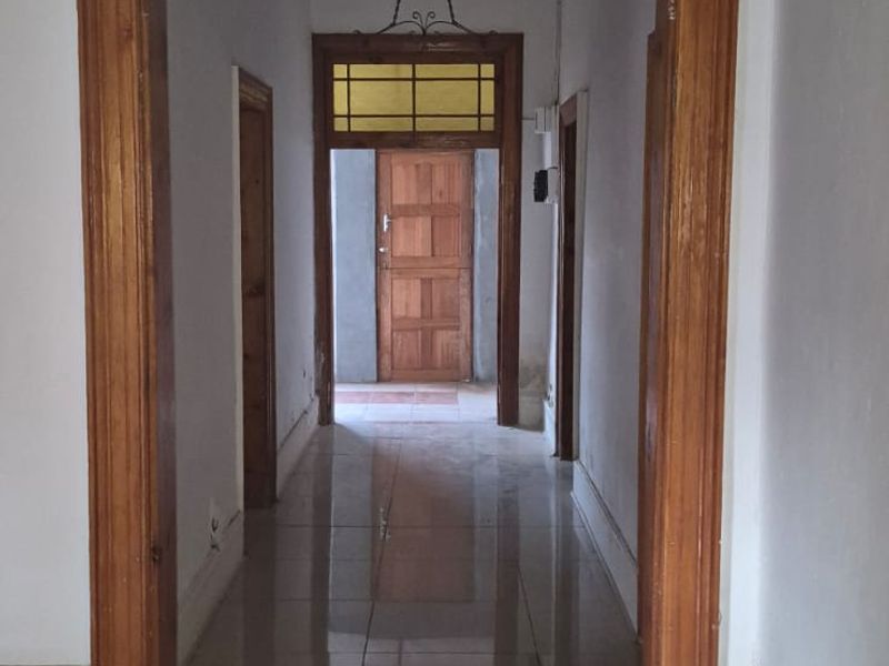 A long, empty hallway featuring tiled flooring, wooden door frames, and a transom window above the rear exit door.