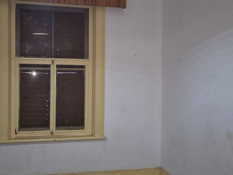 An empty bedroom featuring a timber ceiling, timber window frames, and original skirting boards, requiring cosmetic updates to improve its overall condition.