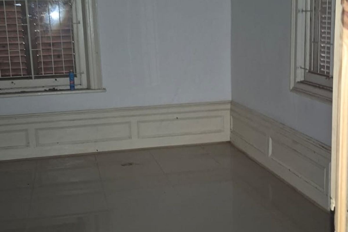 An empty bedroom featuring tiled flooring, wainscoting, and windows fitted with security bars and timber pelmets.