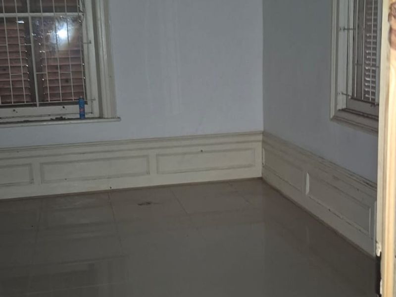 An empty bedroom featuring tiled flooring, wainscoting, and windows fitted with security bars and timber pelmets.