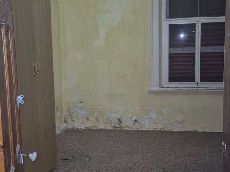 An empty bedroom featuring built-in wardrobes, carpet flooring, and a timber ceiling, currently requiring wall repairs and cosmetic updates.