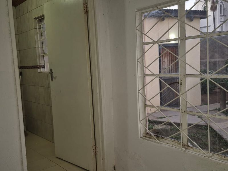 An interior space featuring tiled walls and security bars on the windows, looking out toward an outdoor area with a brick structure.