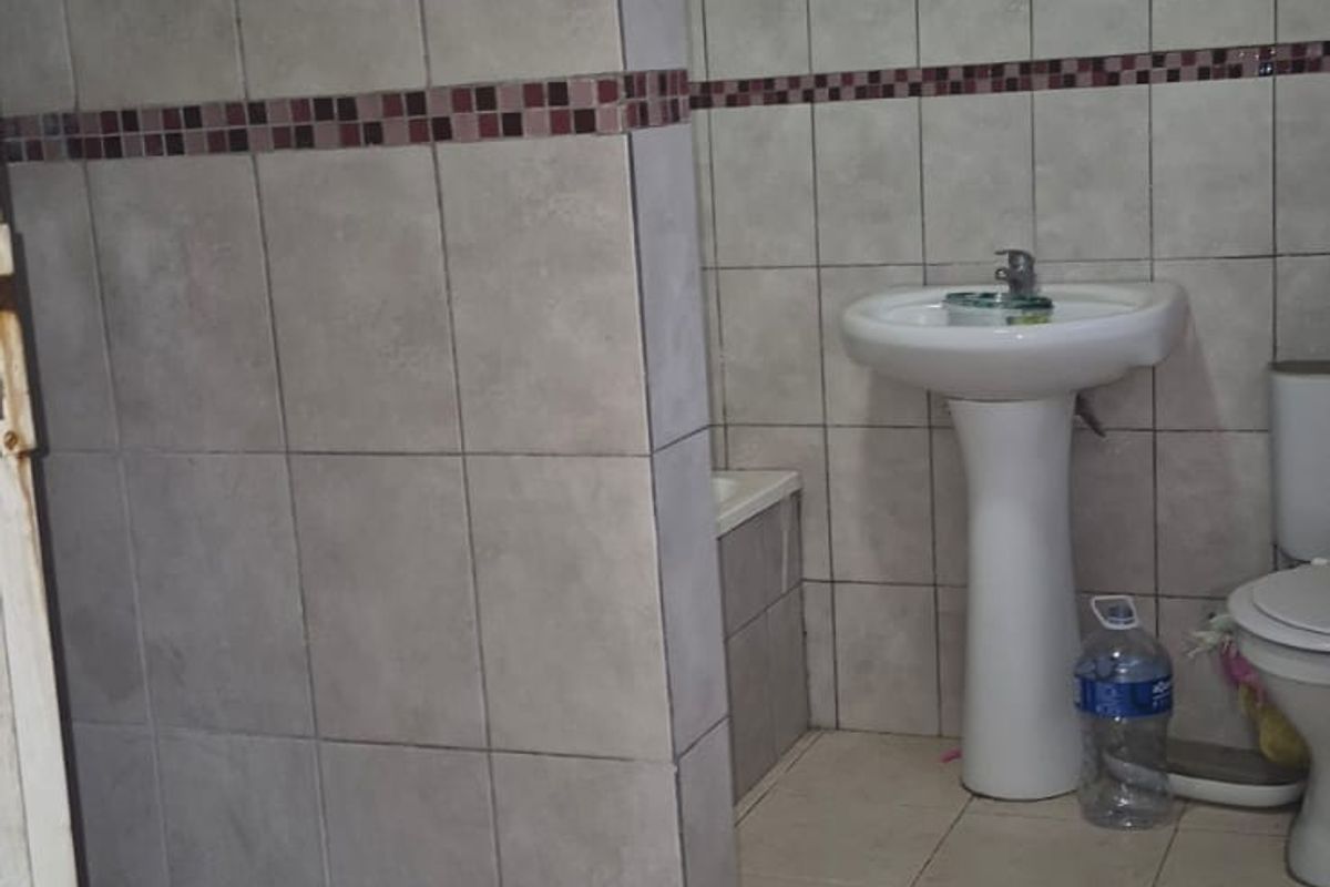 A functional bathroom featuring a pedestal basin, toilet, and a tiled shower enclosure with timber ceiling finishes.