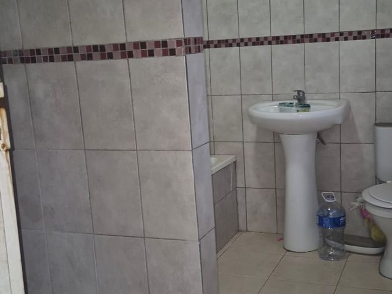 A functional bathroom featuring a pedestal basin, toilet, and a tiled shower enclosure with timber ceiling finishes.
