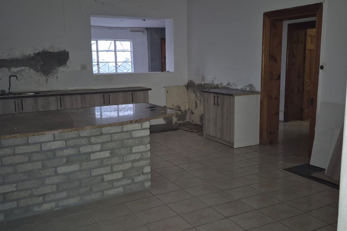 An unfinished kitchen space featuring a brick breakfast bar, tiled flooring, and cabinetry, currently requiring wall repairs and completion of finishes.