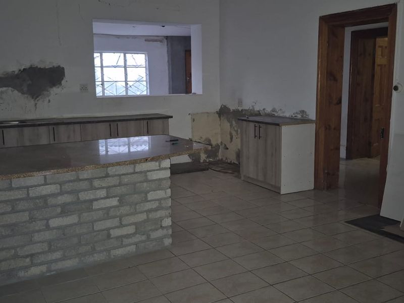 An unfinished kitchen space featuring a brick breakfast bar, tiled flooring, and cabinetry, currently requiring wall repairs and completion of finishes.