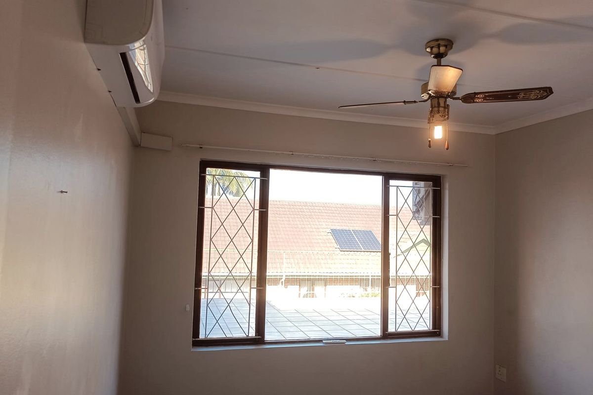 A bright, empty bedroom featuring a ceiling fan, split-system air conditioning unit, and windows fitted with security bars.