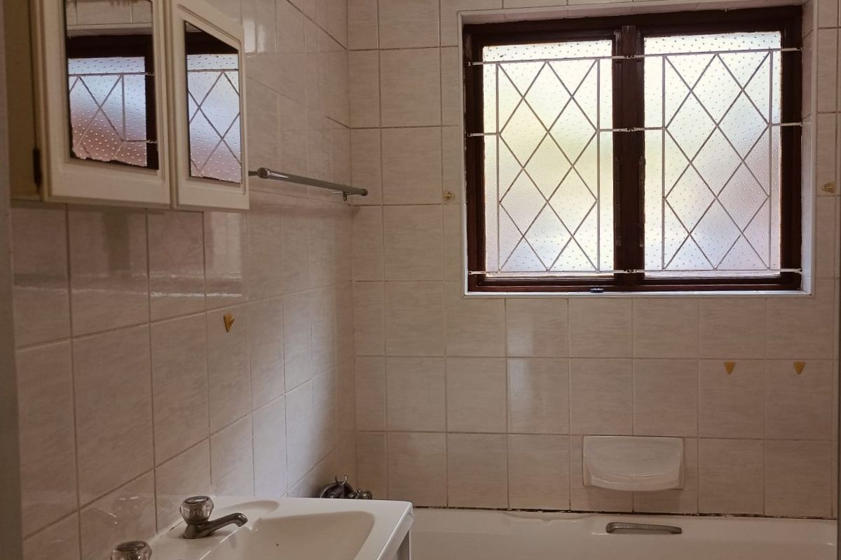 A dated bathroom featuring a built-in vanity, bathtub, and fully tiled walls, offering a functional space ready for modernization and cosmetic updates.