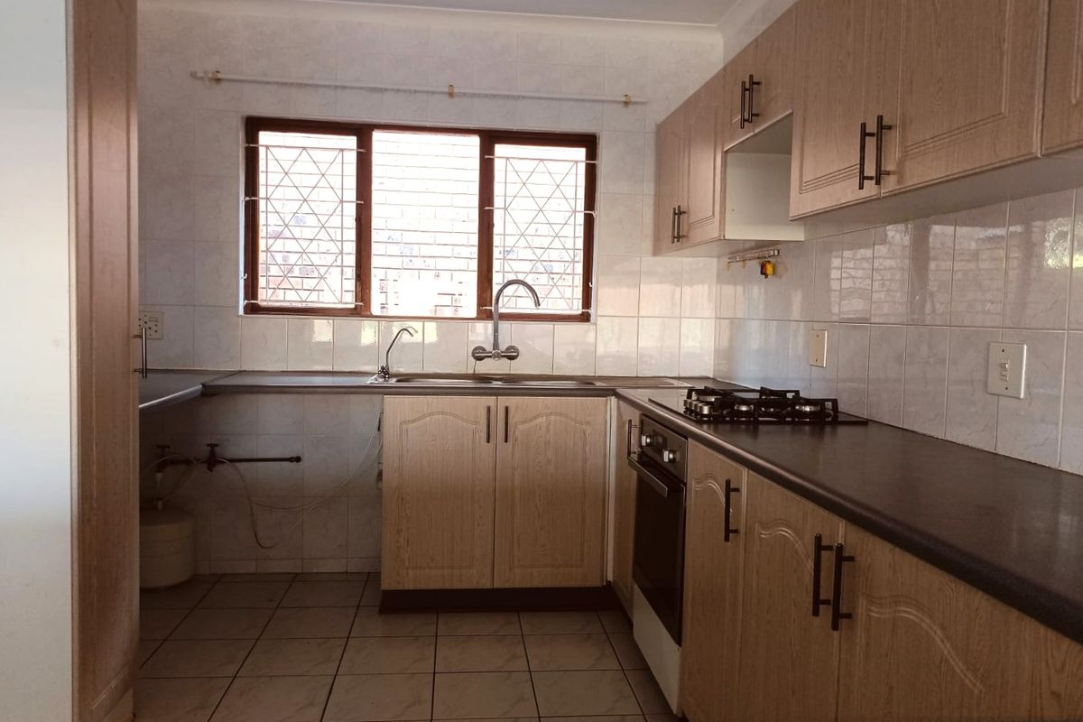 A functional kitchen featuring laminate cabinetry, a built-in oven, gas hob, and tiled backsplash, with security bars installed on the window.