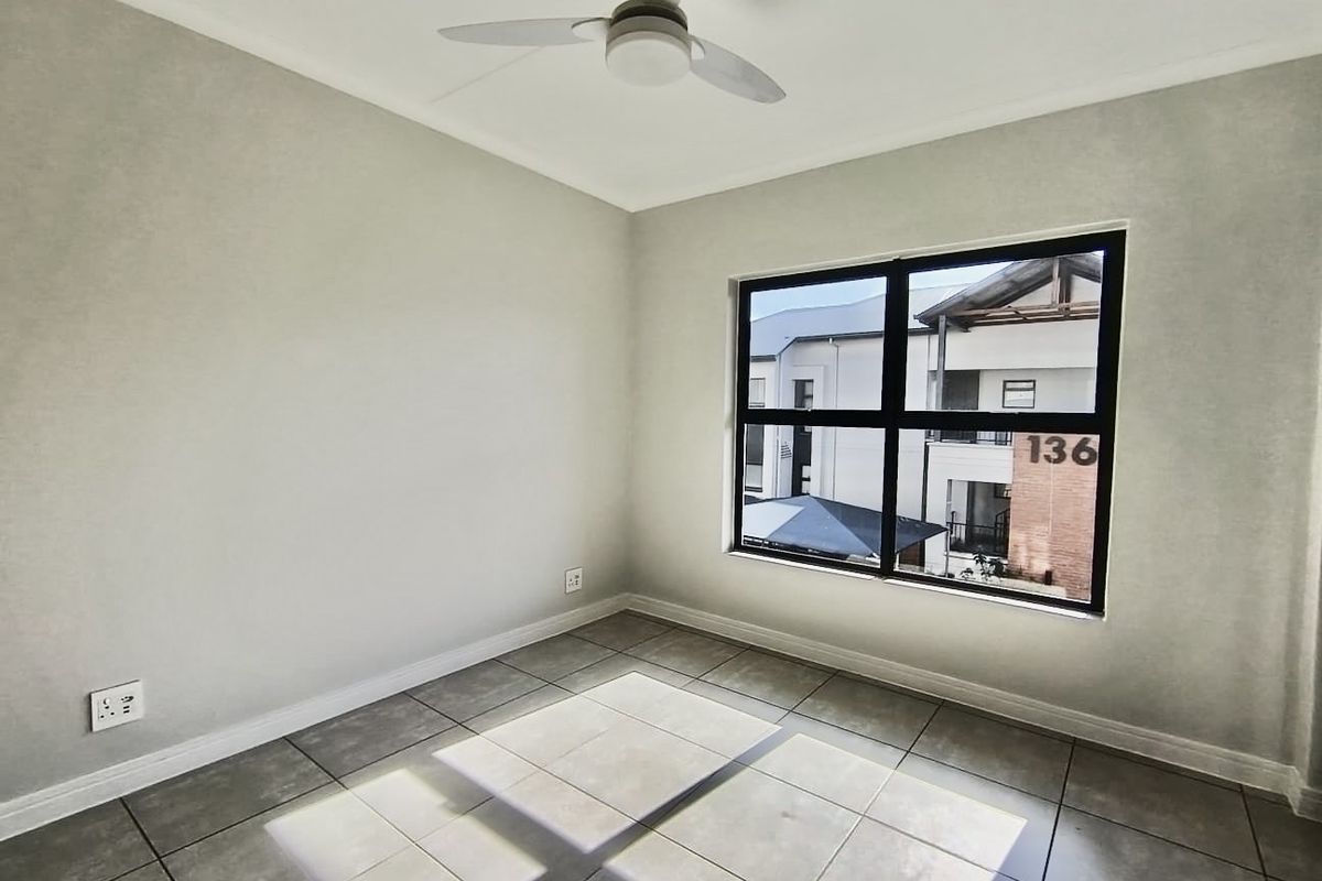 A bright, empty bedroom featuring neutral wall tones, tiled flooring, and a modern ceiling fan, offering a clean canvas for personalization.