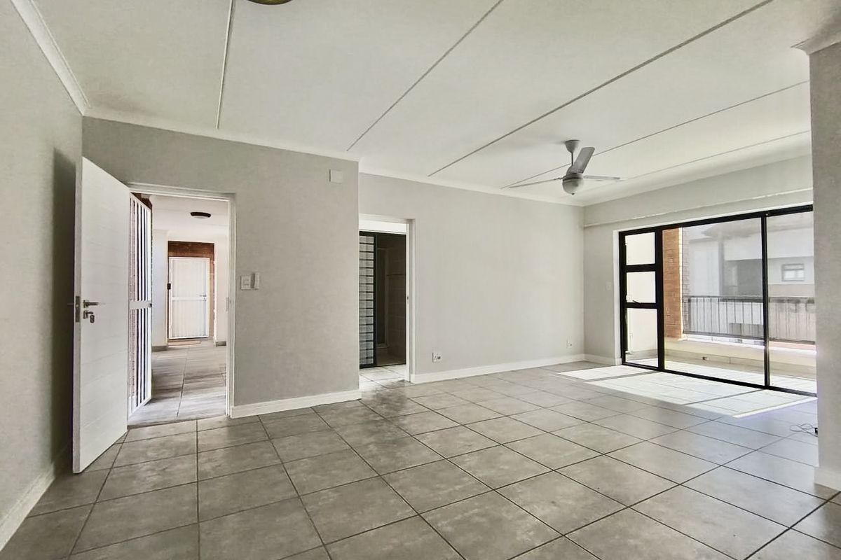 Spacious, light-filled living area featuring neutral tiled flooring, a ceiling fan, and large sliding glass doors leading to an outdoor balcony.