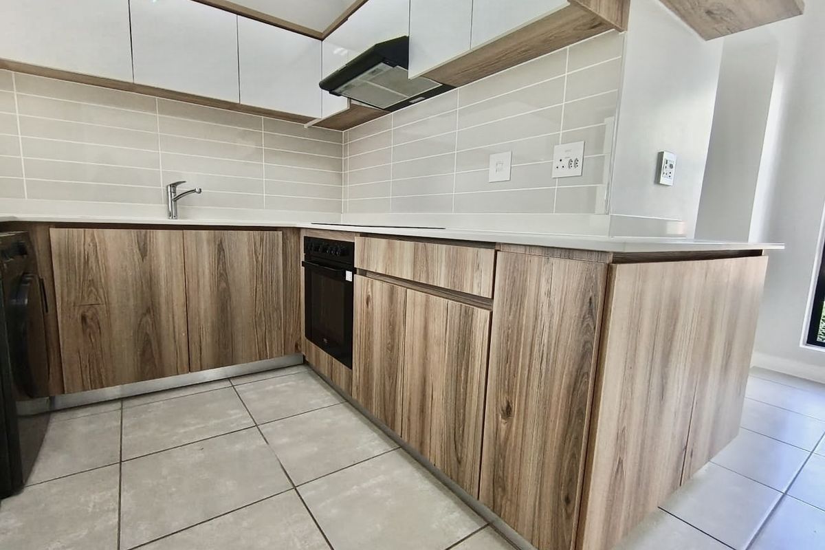Modern kitchen featuring wood-grain cabinetry, white upper cabinets, integrated oven, extractor fan, and neutral tiled flooring in a clean, contemporary layout.