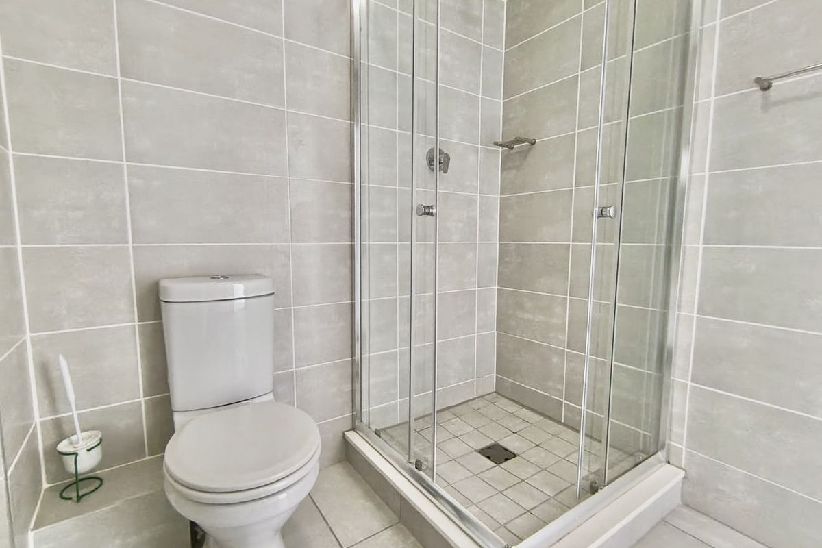 A clean and modern bathroom featuring a glass-enclosed shower and a standard toilet with neutral wall and floor tiling.