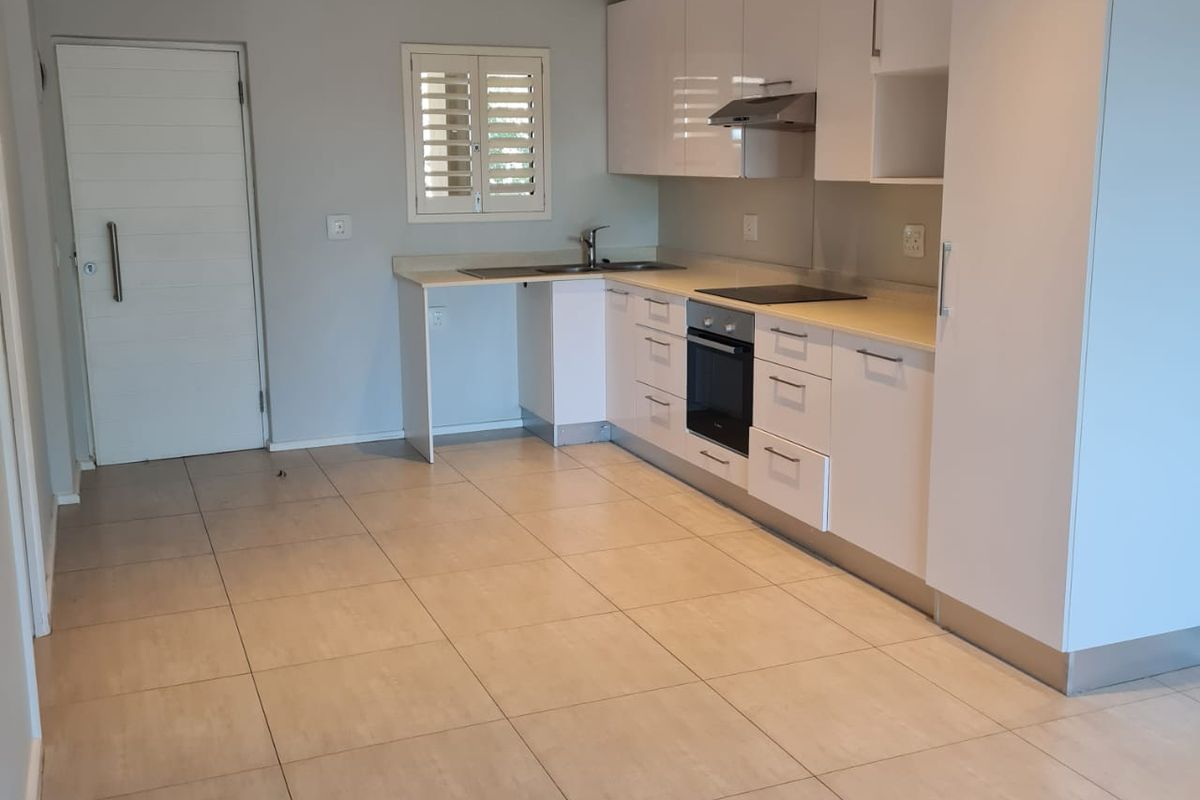 Modern kitchen featuring white high-gloss cabinetry, integrated oven and hob, tiled flooring, and recessed lighting in an open-plan layout.