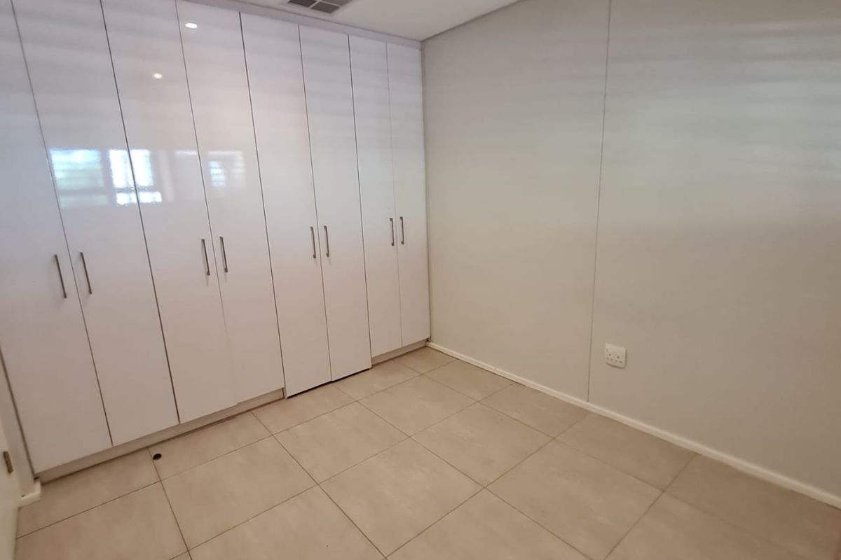 A clean, empty bedroom featuring modern white built-in cupboards, neutral tiled flooring, and recessed ceiling lighting.