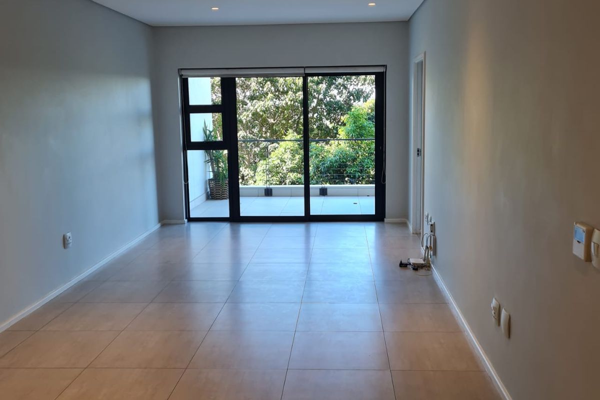 A bright, empty living room featuring neutral tiled flooring, recessed lighting, and large sliding glass doors that open onto a private balcony.