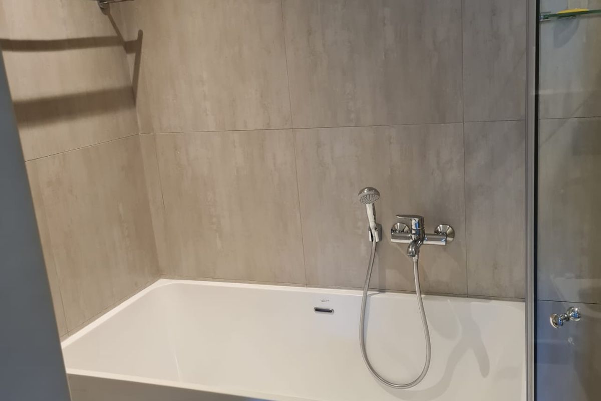 A modern bathroom featuring a clean freestanding bathtub, wall-mounted shower fixtures, and neutral-toned wall tiling.