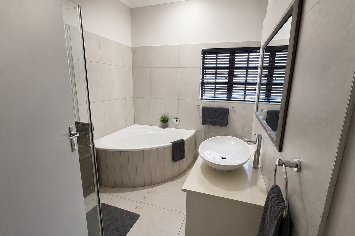 Modern bathroom featuring a corner bathtub, vessel sink on a vanity cabinet, and neutral wall tiling with contemporary fixtures.