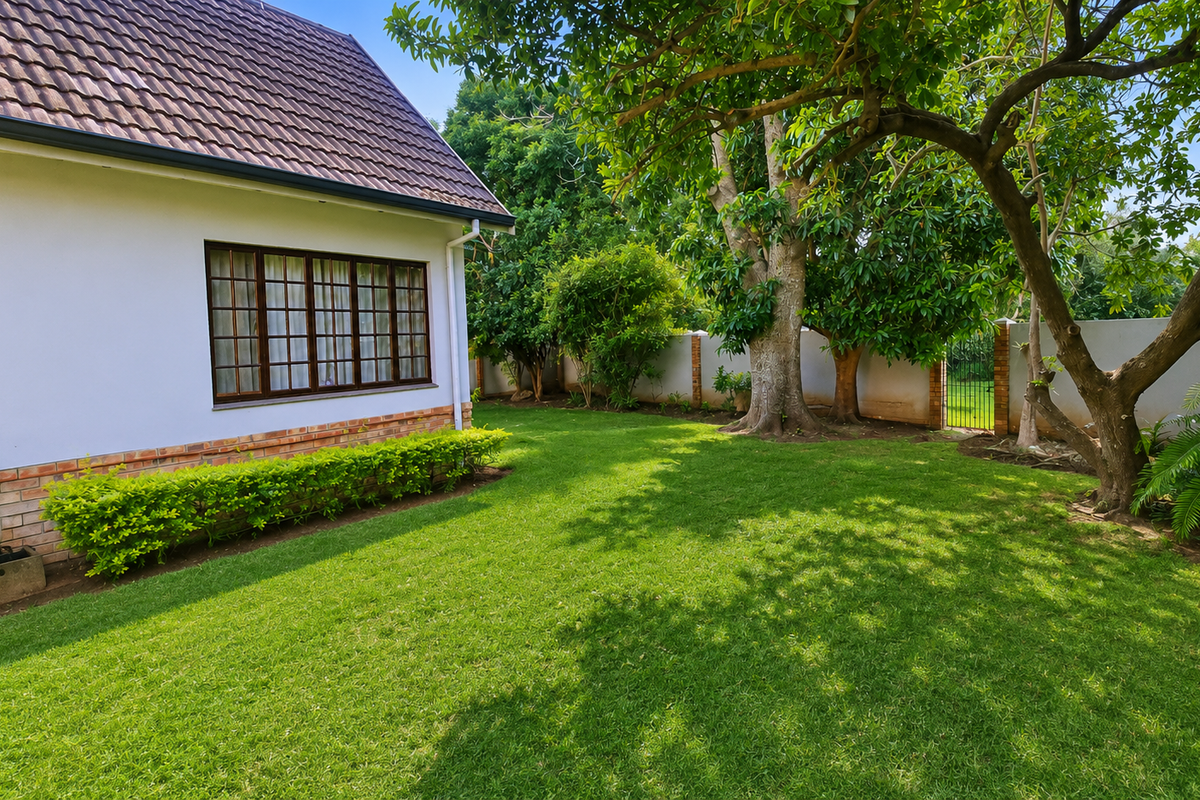 A well-maintained rear garden featuring a lush lawn, mature trees, and a cottage exterior with a tiled roof and brick detailing.