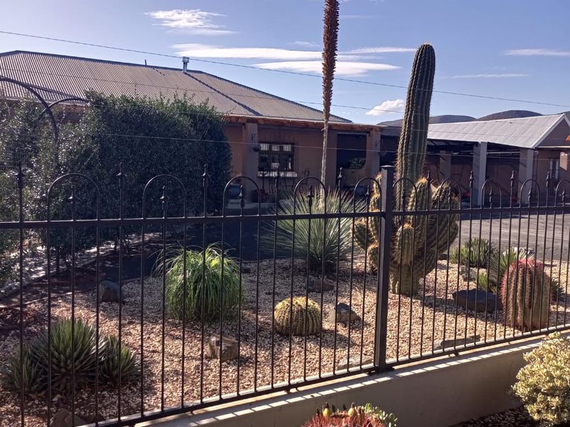 Front view of the property featuring a metal perimeter fence, gravel landscaping with established cacti, and a corrugated metal roof structure.