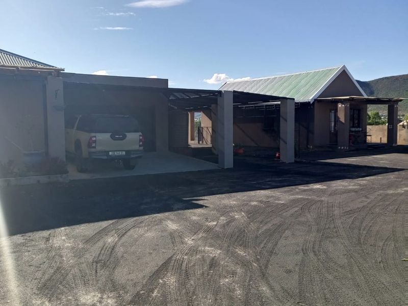 Front exterior view of the property featuring a large asphalt driveway, attached garage, and covered carport area under a metal roof.