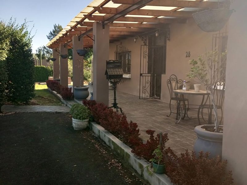 A covered patio area featuring a timber pergola with corrugated roofing, tiled flooring, and secure wrought iron fixtures overlooking the garden.