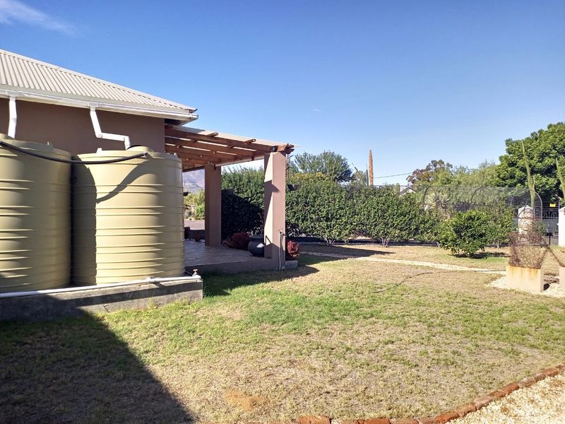 Rear garden area featuring a covered patio with timber pergola and large water storage tanks connected to the building's gutter system.
