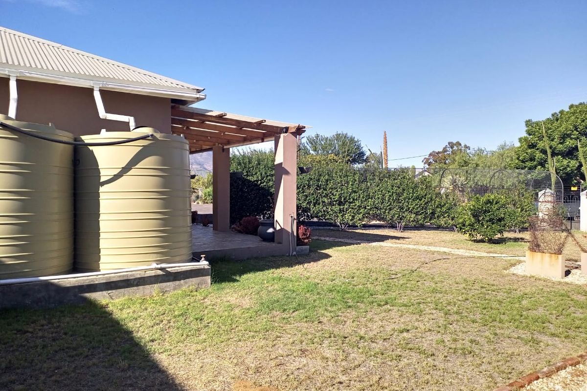 Rear garden area featuring a covered patio with timber pergola and large water storage tanks connected to the building's gutter system.