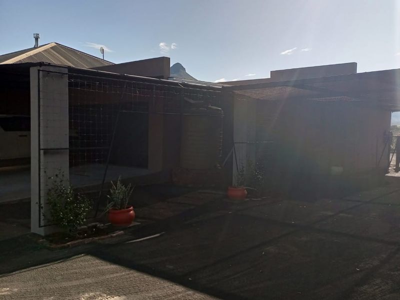 Front exterior view of the property featuring a covered carport area, concrete driveway, and a water tank installation.