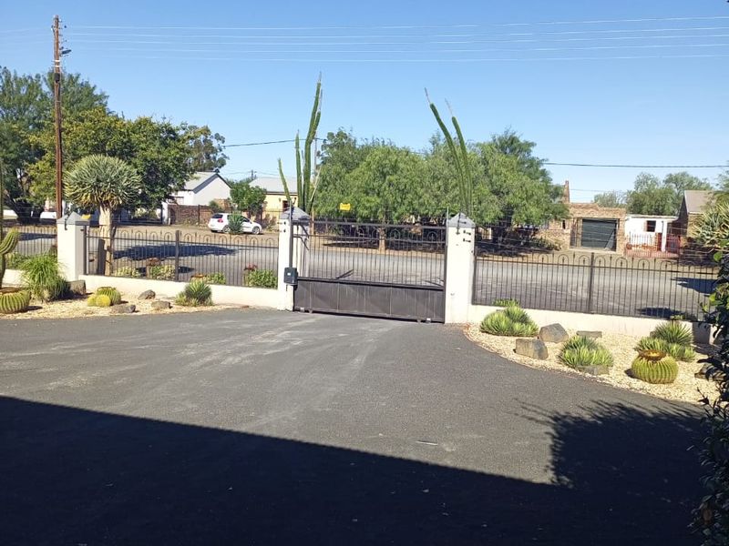 A secure front entrance featuring an automated sliding gate, masonry pillars, and metal perimeter fencing leading onto a paved asphalt driveway.