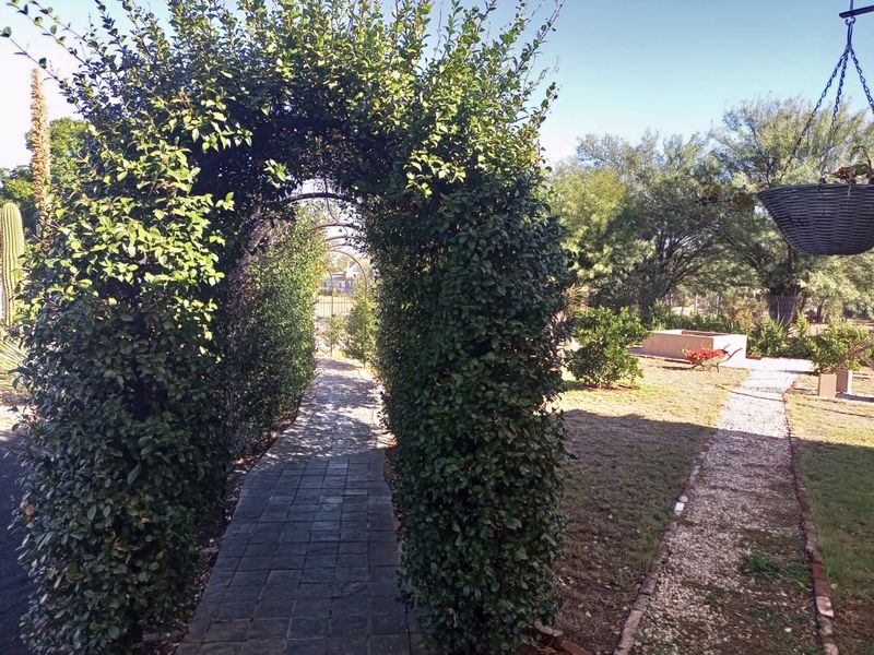 A landscaped garden featuring a paved walkway through a metal archway, gravel paths, and established hedging.
