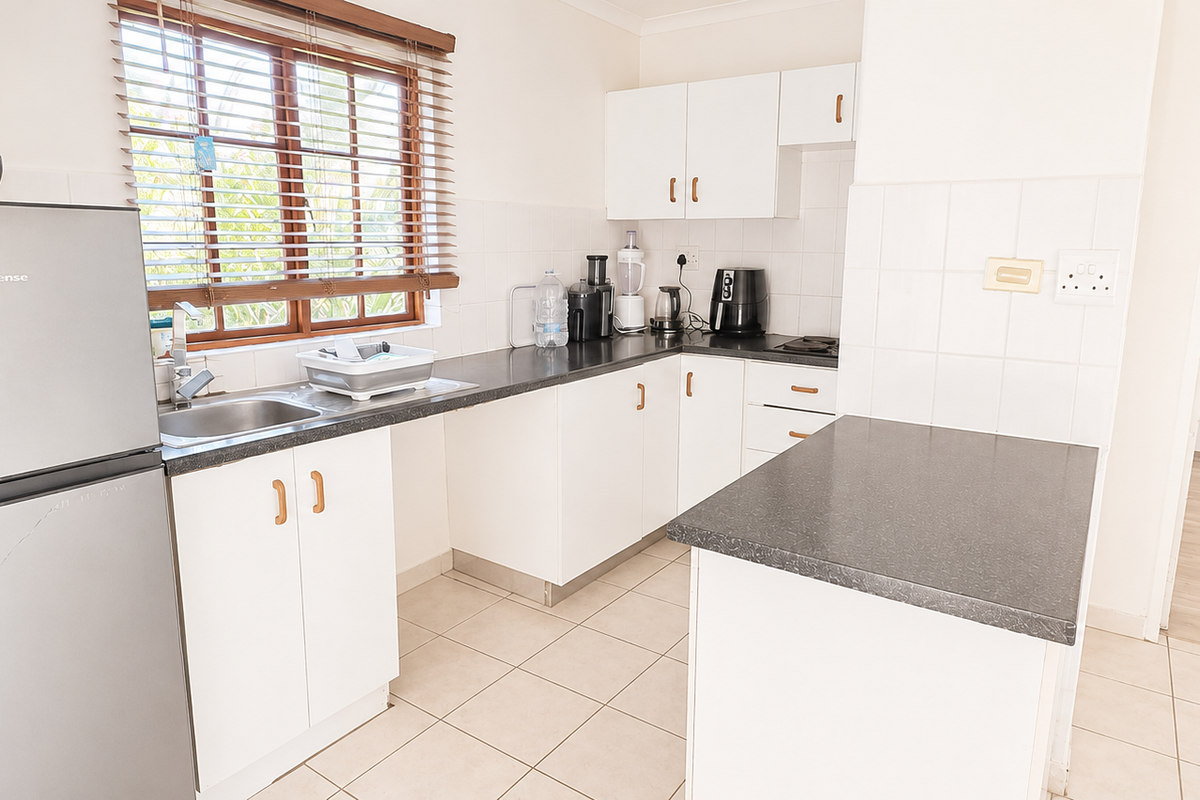 A functional kitchen featuring white cabinetry, dark laminate countertops, tiled backsplash, and ceramic flooring, offering a clean and practical workspace.