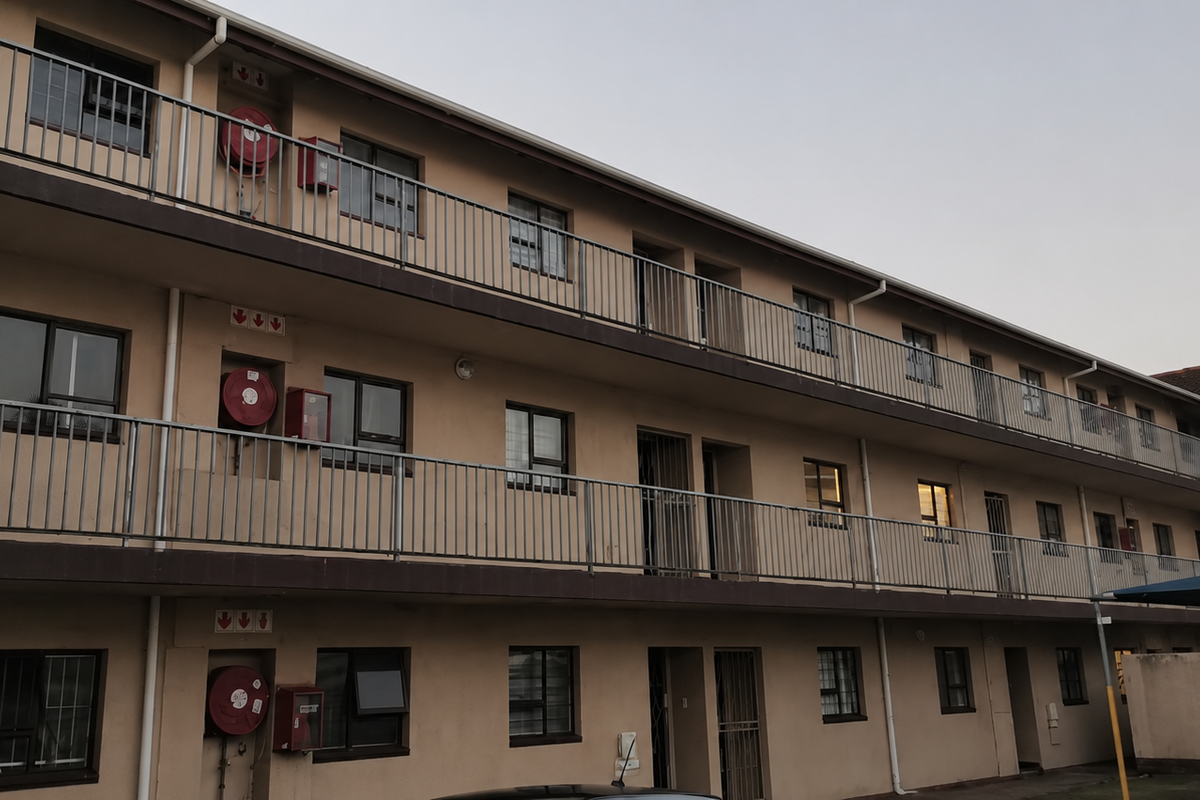 Exterior view of a multi-story apartment block featuring open walkways with metal balustrades, fire safety equipment, and security-fitted windows.