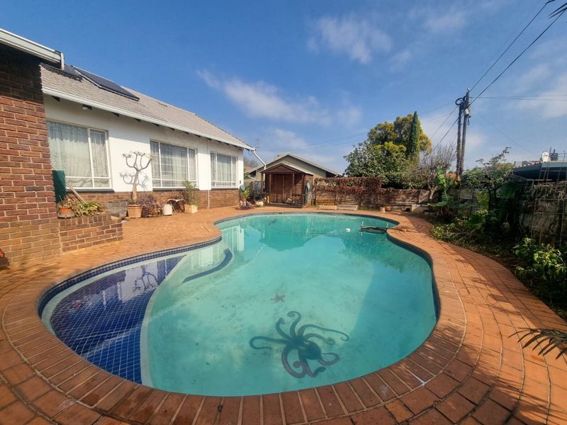 Outdoor pool area featuring a curved swimming pool with brick paving, adjacent to the main house structure and a small garden shed.