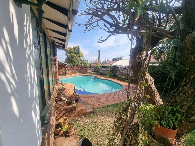 Outdoor pool area featuring a swimming pool with brick paving surround, adjacent to the main house structure with large sliding glass doors.