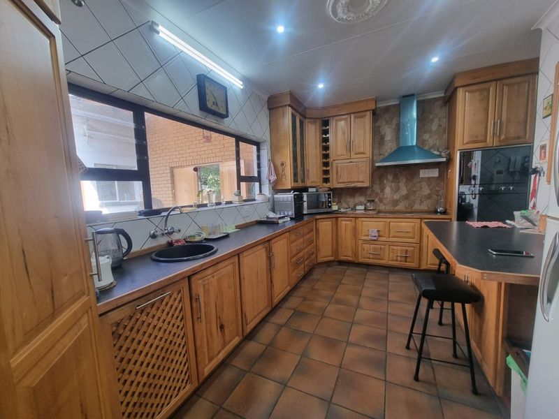 A functional kitchen featuring extensive wooden cabinetry, dark laminate countertops, a breakfast bar, and built-in appliances with tiled flooring and backsplash.