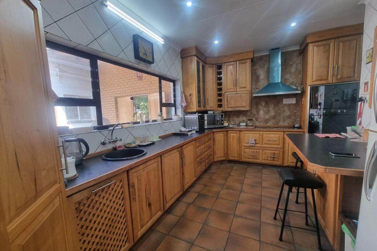 A functional kitchen featuring extensive wooden cabinetry, dark laminate countertops, a breakfast bar, and built-in appliances with tiled flooring and backsplash.