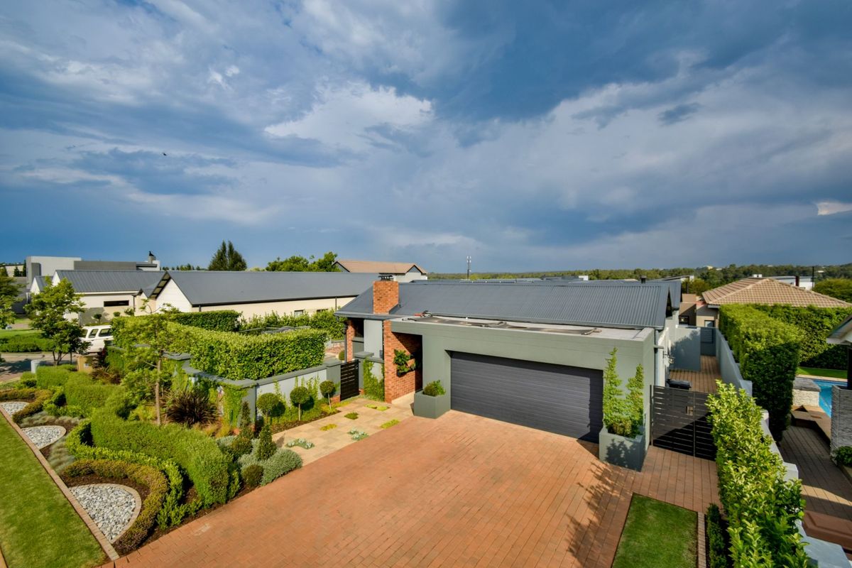 An elevated aerial view of the property featuring a brick driveway, double garage, and well-maintained landscaped gardens with mature hedging.