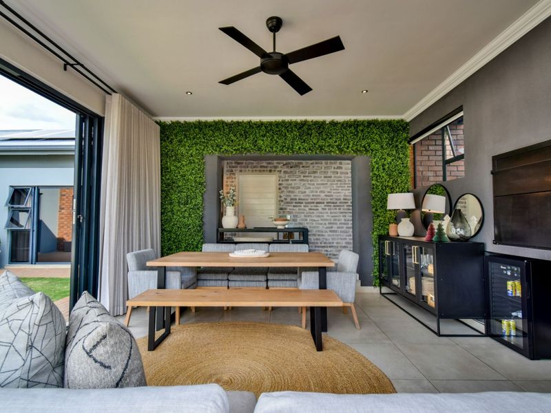 A modern covered patio featuring an exposed brick and artificial green feature wall, recessed lighting, ceiling fan, and large stacking doors opening to the garden.